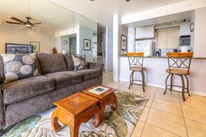 Una sala de estar con sofá, mesa de centro y una zona de cocina con barra y taburetes.