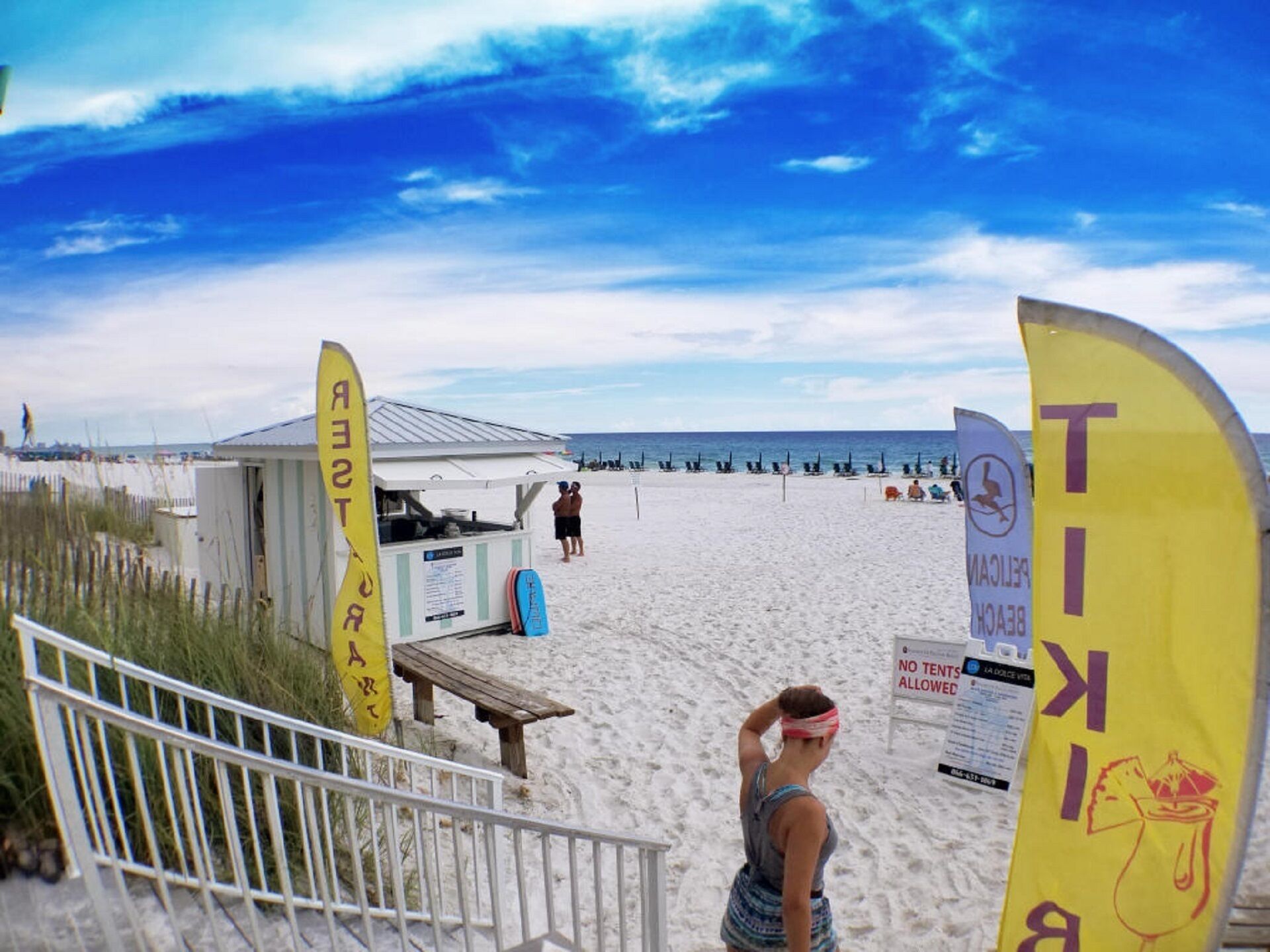 Une scène de plage avec un poste de surveillance des sauveteurs, des parasols et un panneau interdisant l’installation de tentes.