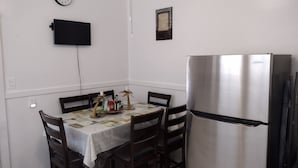 A small dining area with a table set for four, a stainless steel refrigerator, and a wall-mounted TV.