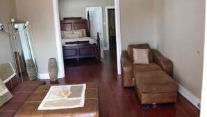 A living room with a brown leather sofa, a brown leather ottoman, a wooden bed with a headboard, and a mirror with lights.