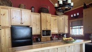 A kitchen with wooden cabinets, a black refrigerator, a microwave, and a fruit bowl on the counter. - Charming Mountain Cabin (Angel Fire)