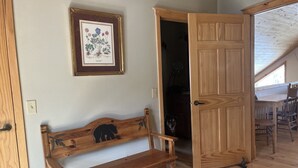 A wooden bench with a bear design, a wooden door, and a framed botanical illustration on the wall. - Charming Mountain Cabin (Angel Fire)