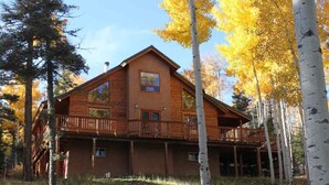 A log cabin with a balcony and a large window, surrounded by trees with yellow leaves. - Charming Mountain Cabin (Angel Fire)