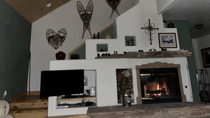 A living room with a fireplace, a TV, and decorative wall art. - Charming Mountain Cabin (Angel Fire)