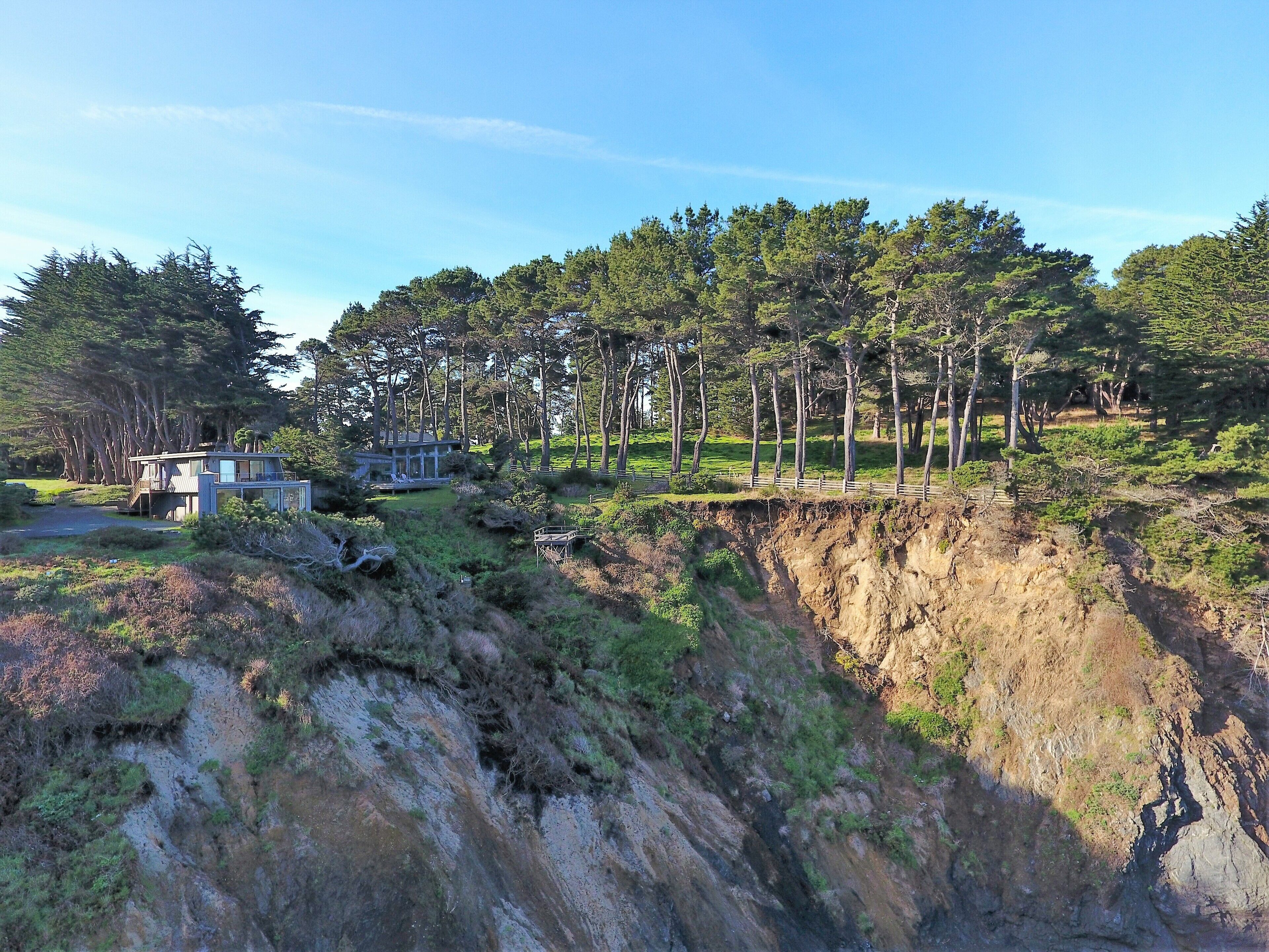 Une maison moderne dotée d’une grande terrasse, entourée d’une forêt dense et d’une falaise abrupte.