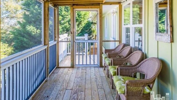 A covered porch with a wooden floor, wicker chairs with green cushions, and a view of a backyard.
