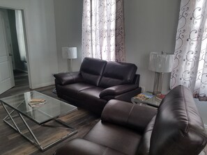 Ein Wohnzimmer mit einer dunkelbraunen Ledersofa, einem Glastisch und einer Lampe.