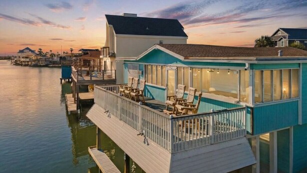 A waterfront property with a dock, a covered deck with seating, and a building with large windows. - Canal Front Home with Private Pool & Boat Slip (Galveston)