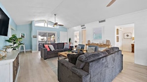 A spacious living room with a gray sofa, a coffee table, and a ceiling fan. - Canal Front Home with Private Pool & Boat Slip (Galveston)