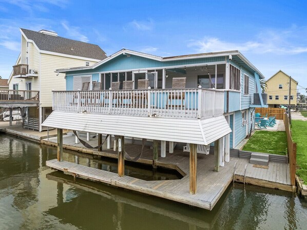A waterfront house with a dock, a covered deck, and a small yard.