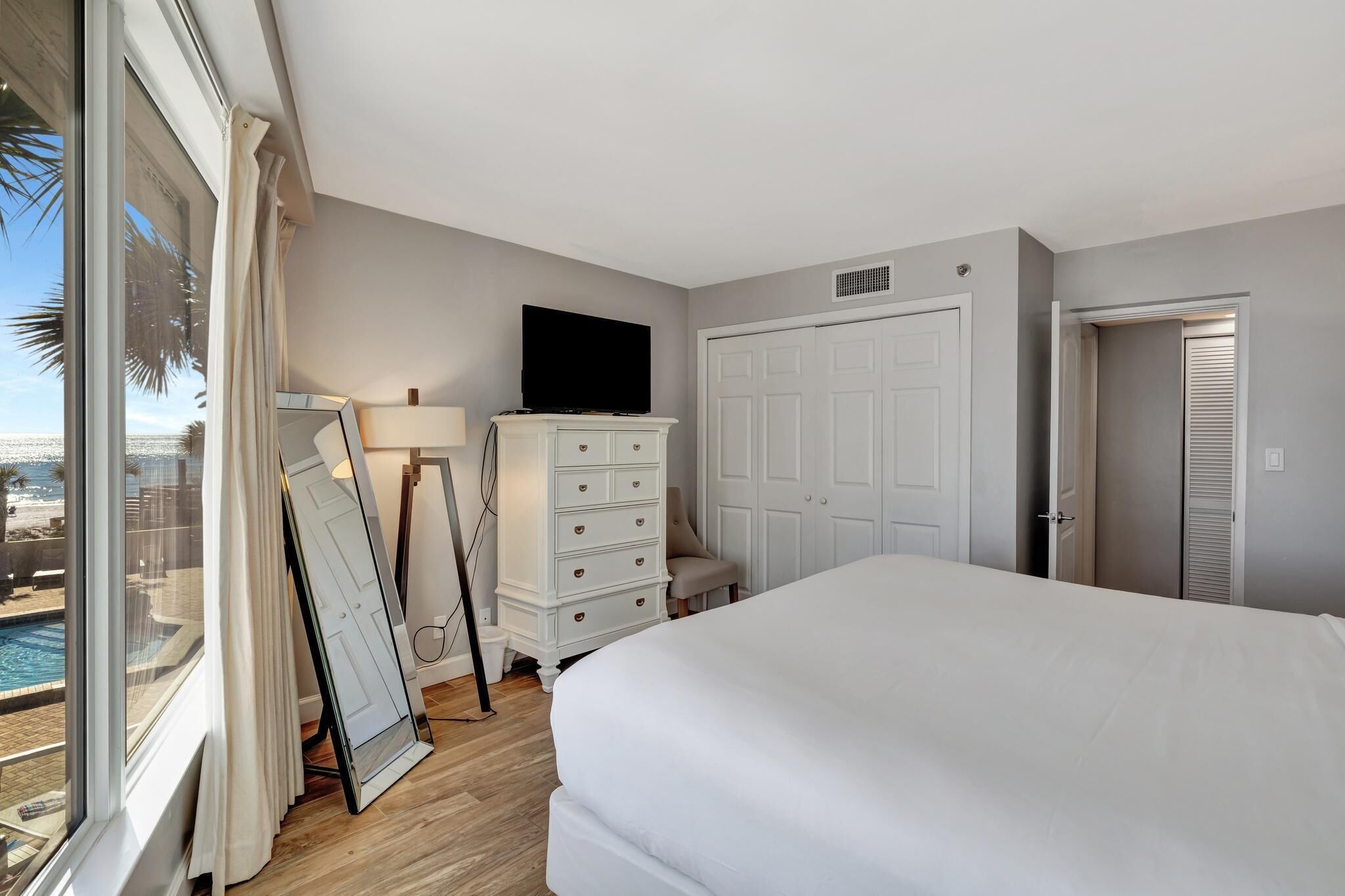 Une chambre avec un grand lit, une commode, une télévision et une vue sur une piscine.