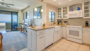 A modern kitchen with white cabinets, a built-in microwave, and a large oven. There is a dining area with a table and chairs, and a balcony with a view. - KGV 24T8  Spacious 1BD Oceanview Villa (Lahaina)