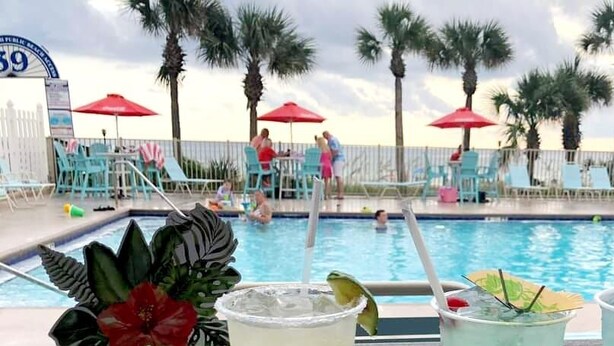 A pool area with lounge chairs, umbrellas, and palm trees. - 153 Grand Island Blvd ~ Total Reno~Custom Kitchen~Granite~WiFi (Panama City Beach)