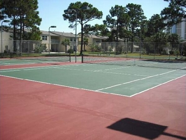 An outdoor tennis court with a net, surrounded by trees and buildings.