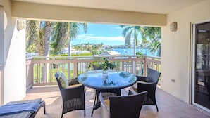 A round table with chairs on a balcony, overlooking a marina with boats and palm trees.