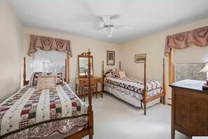Un dormitorio con dos camas individuales, un escritorio de madera, una silla, un armario y un ventilador de techo.