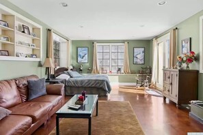 A spacious living room with a brown leather sofa, a glass coffee table, and a bed with a grey bedspread. - Views of Catamount!  Tanglewood, Skiing, Bash Bish Falls, Barn At Liberty Farms! (Hillsdale)