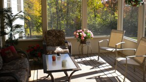 Ein Wintergarten mit Blick auf Herbstbäume, Korbmöbel und einem Tisch mit Getränken.