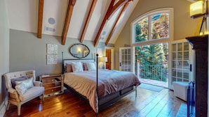 Une chambre à coucher avec un grand lit, une chaise, une commode et une fenêtre donnant sur les arbres.