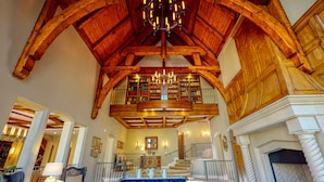 Un intérieur spacieux avec un haut plafond en bois, une cheminée, un escalier et une bibliothèque dotée d’étagères.