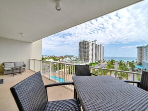 Uma varanda com móveis de vime, piscina e vista para edifícios altos e o oceano.
