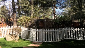 Une cour arrière clôturée avec une terrasse en bois, un petit jardin et un chemin en pierre.