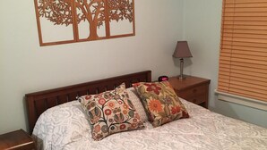 Une chambre à coucher comprenant un lit, deux tables de chevet, un élément de décoration murale, une lampe et une fenêtre avec des stores.