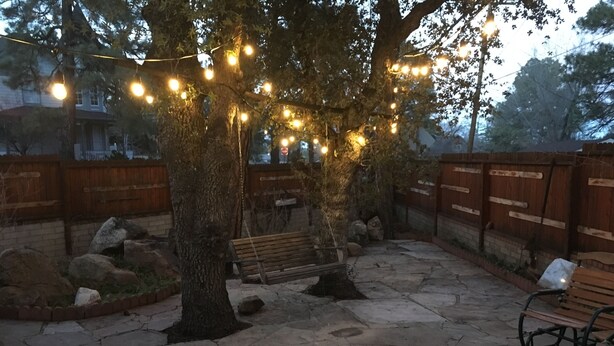 Un espace extérieur aménagé en terrasse, avec un sol en pierre, des bancs en bois et des guirlandes lumineuses.