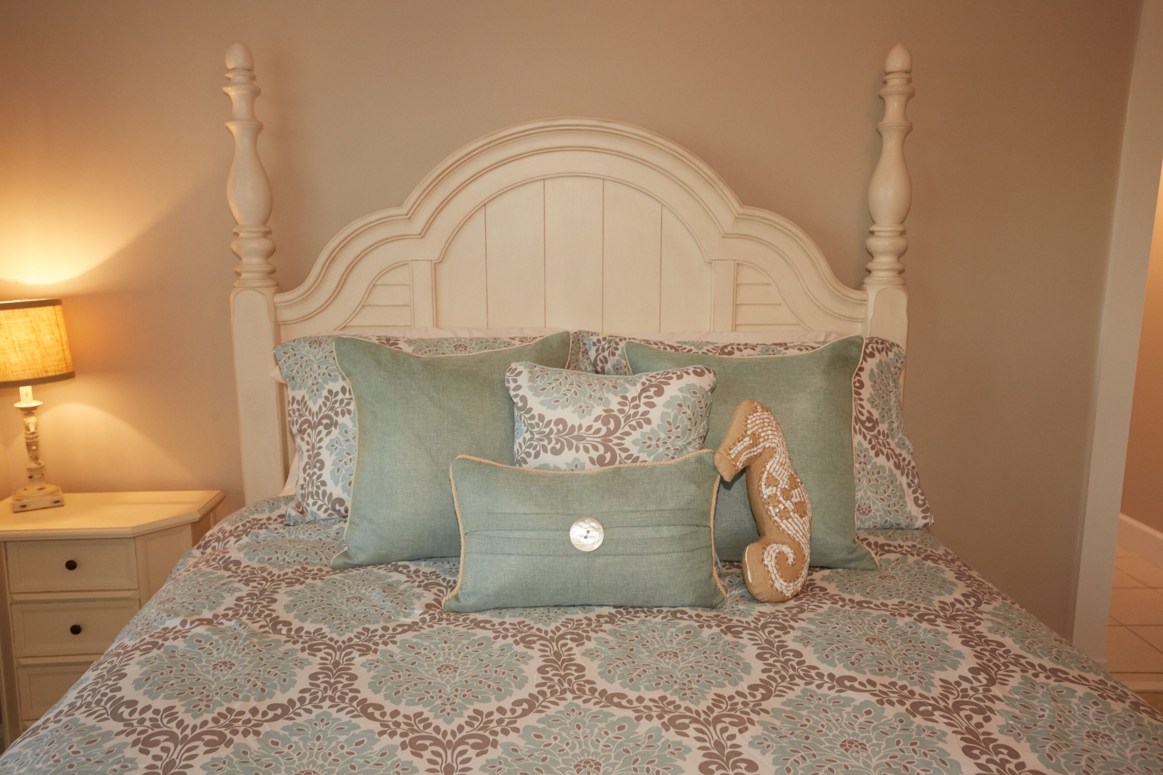 A bed with a white headboard, multiple pillows with floral patterns, and a nightstand with a lamp.