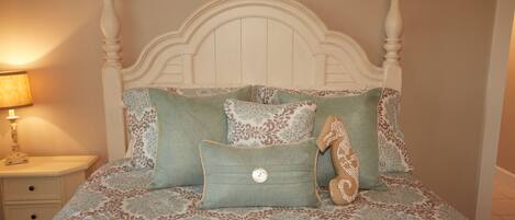 A bed with a white headboard, multiple pillows with floral patterns, and a nightstand with a lamp.