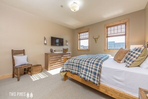 A bedroom with a wooden bed, a dresser, a chair, a television, and a window with a city view.