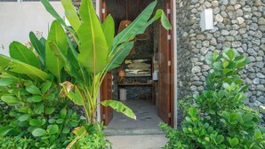 A stone wall entrance with a wooden door, a concrete pathway, and lush green foliage. - Modern Family Home w/pool, steps to beach in private community (Guanacaste Province)