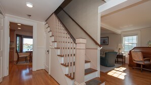 Un escalier avec des marches en bois et une rampe de couleur beige mène au deuxième étage. On aperçoit à l’arrière-plan un coin repas avec une table et des chaises.