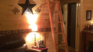 A wooden cabin interior with a loft bedroom, a wooden ladder, a leather chair, a small table with a lamp, and a star decoration on the wall. - 2BR +loft  Cottage in the mountains Va Creeper Trail, HOT TUB, ATV rentals,  (Mountain City)