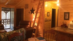 A cozy cabin interior with a wooden interior, a dining area, a living room with a leather couch, and a staircase leading to an upper level. - 2BR +loft  Cottage in the mountains Va Creeper Trail, HOT TUB, ATV rentals,  (Mountain City)