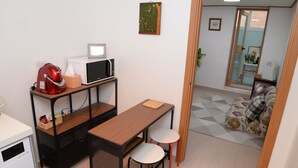 Ein kompakter Wohnraum mit Küchenzeile, einem Essbereich mit Tisch und zwei Stühlen, einer kleinen Couch und einer Schiebetür zu einem weiteren Raum.