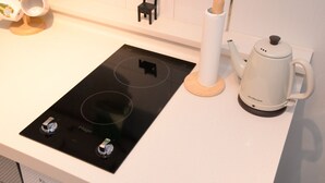 Eine Küche mit einem schwarzen Induktionskochfeld, einem weißen Wasserkocher und einem kleinen schwarzen Stuhl an der Wand.