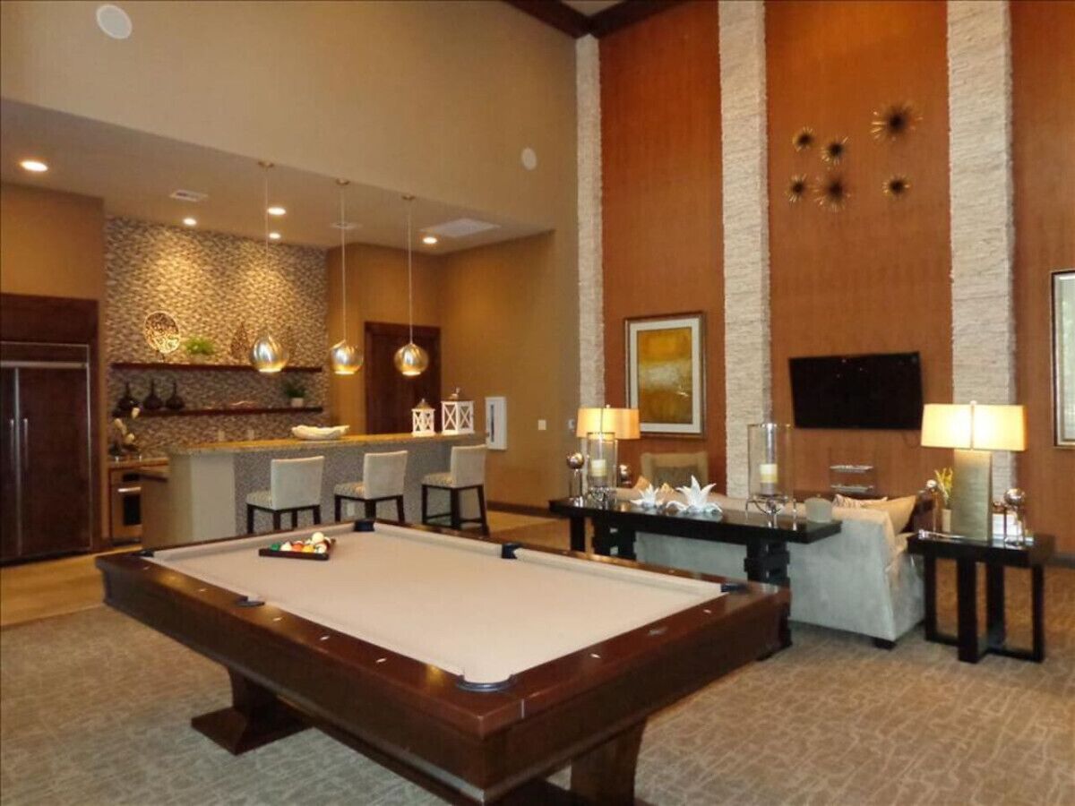 A pool table in a room with a bar area, seating, and a television.