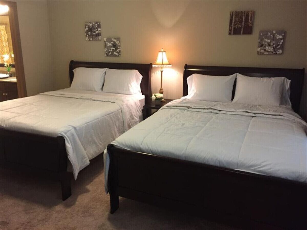 Dos camas individuales con cabeceros de madera oscura y ropa de cama blanca, una mesita de noche con lámpara y decoración en la pared.