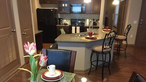 A dining area with a table set for two, a vase of tulips, and a kitchen in the background. - Beautiful Large 2 Bedroom / 2 Bath Condo in The Wo (The Woodlands)
