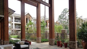 An outdoor patio area with wooden pillars, black wicker furniture, and potted plants. - Beautiful Large 2 Bedroom / 2 Bath Condo in The Wo (The Woodlands)