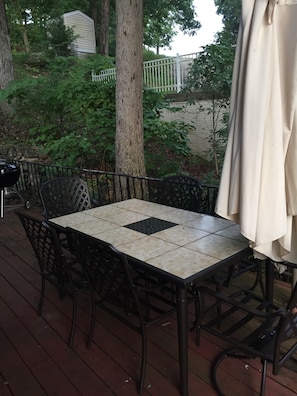 Relax on the outdoor patio with a table and six chairs, surrounded by a deck and lush greenery.