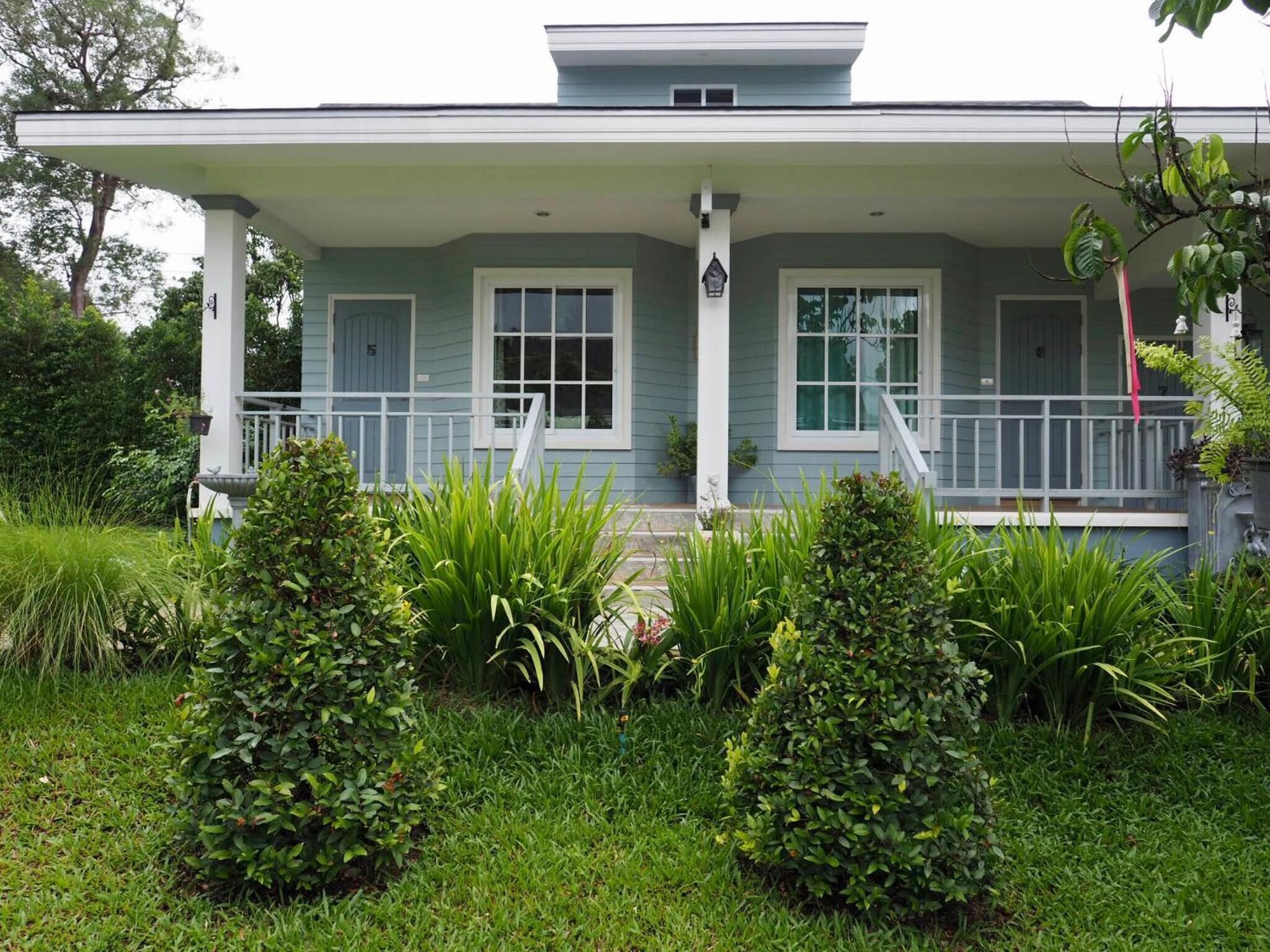 A two-story house with a covered porch, a front entrance, and a small garden area with bushes and grass.