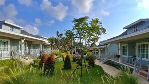 A two-story building with a central garden area, surrounded by a well-maintained lawn and various shrubs. - Little Cottage (Chanthaburi)