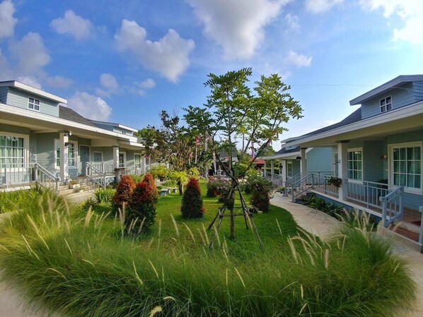 A two-story building with a central garden area, surrounded by a well-maintained lawn and various shrubs. - Little Cottage (Chanthaburi)