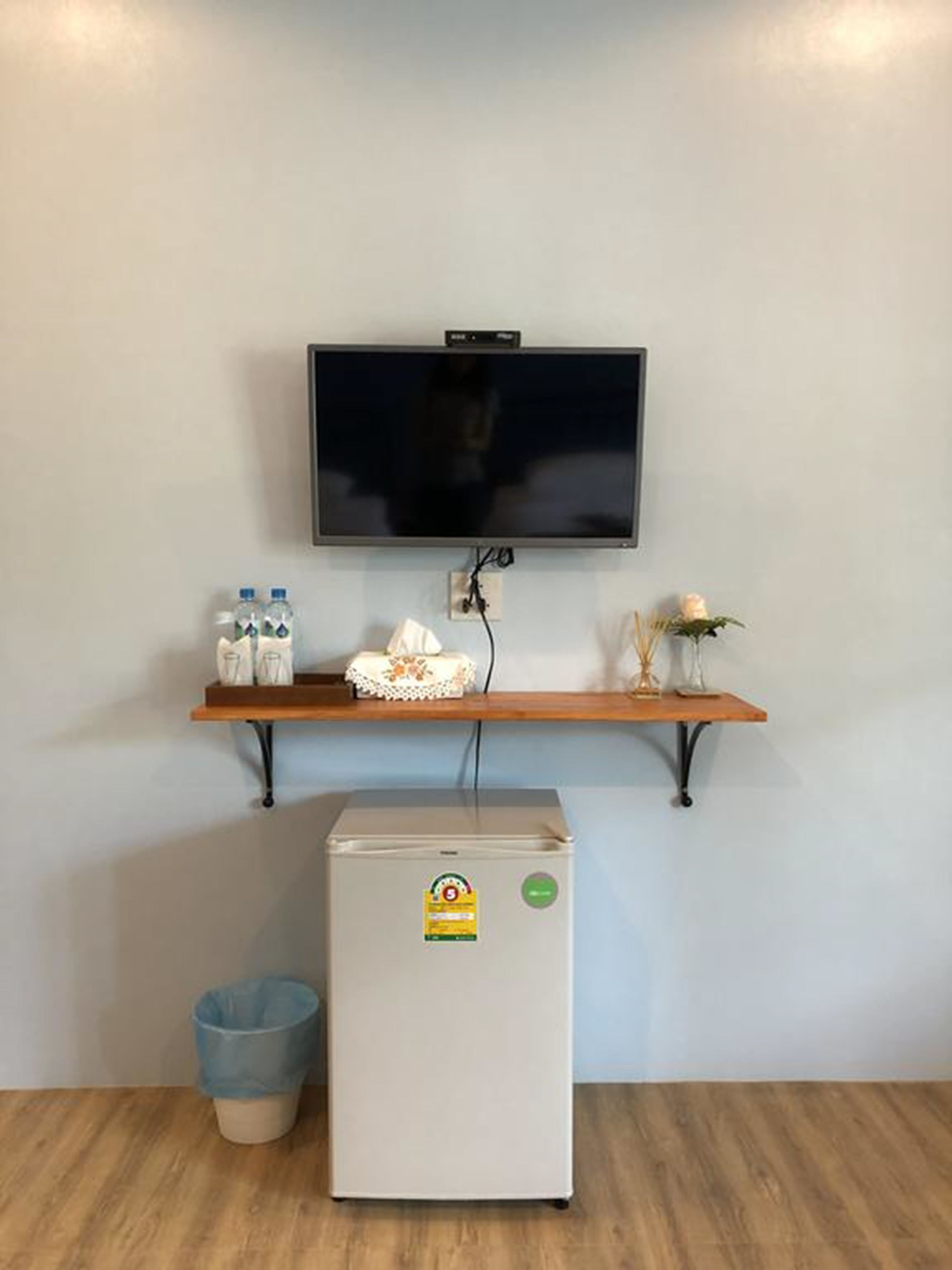 Une petite cuisine équipée d’un réfrigérateur, d’un four à micro-ondes, d’une étagère avec des bouteilles et une boîte de mouchoirs, et d’un téléviseur fixé au mur.