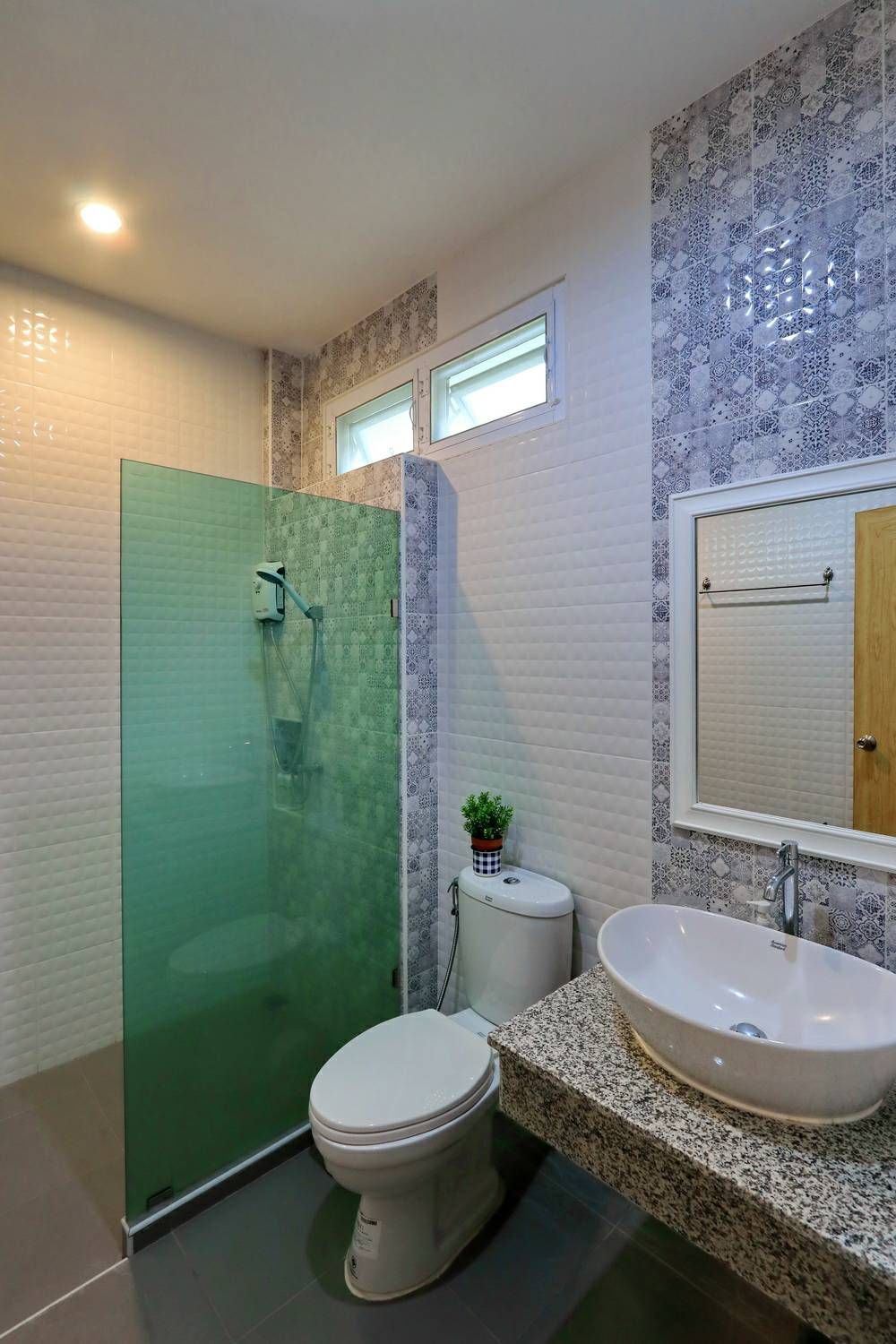 A modern bathroom with a glass shower enclosure, a toilet, a sink with a mirror, and patterned wall tiles.