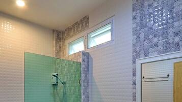 A modern bathroom with a glass shower enclosure, a toilet, a sink with a mirror, and patterned wall tiles.