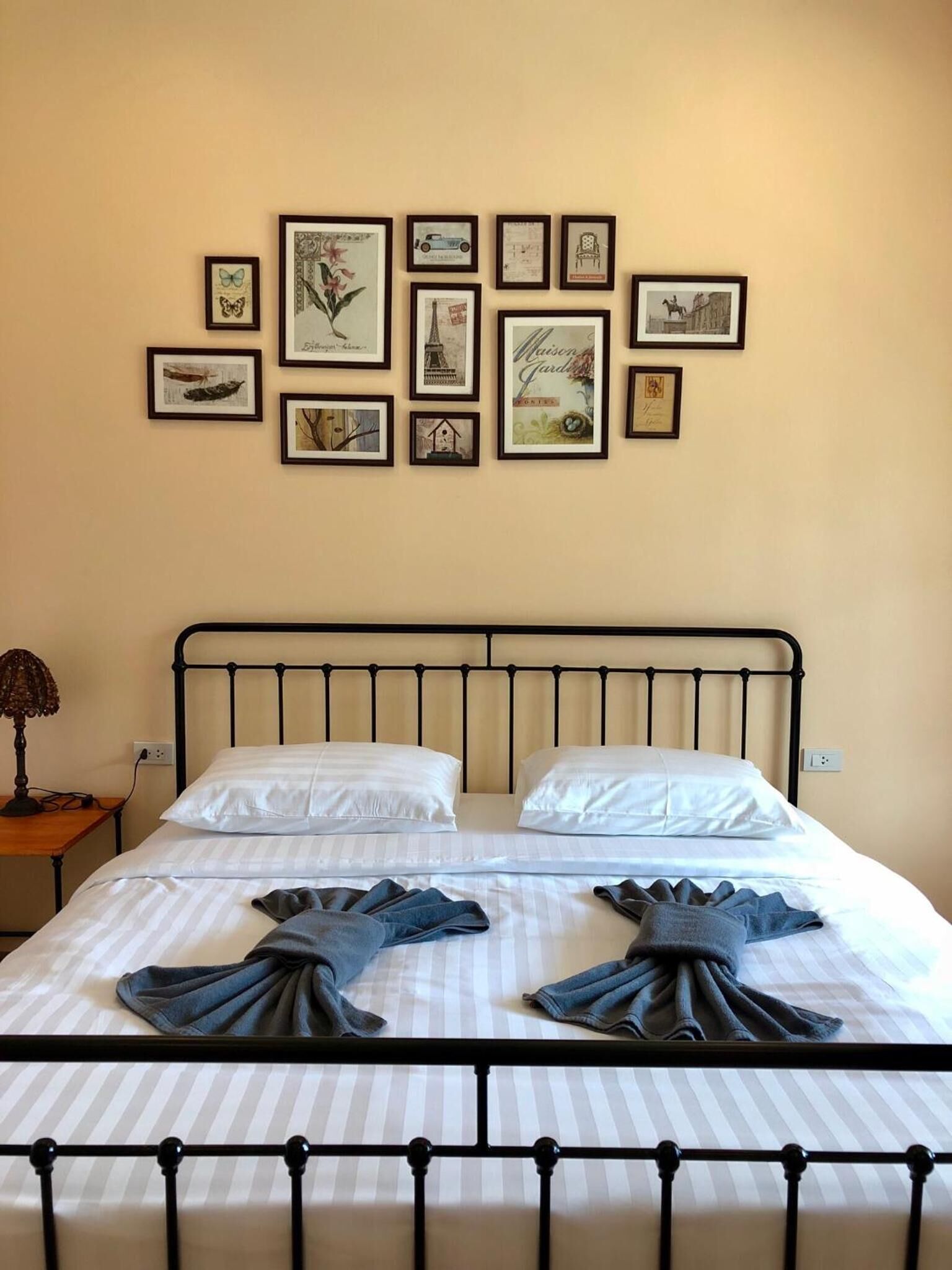 A neatly made bed with white linens and two folded towels, a metal headboard, and a wall adorned with framed pictures.
