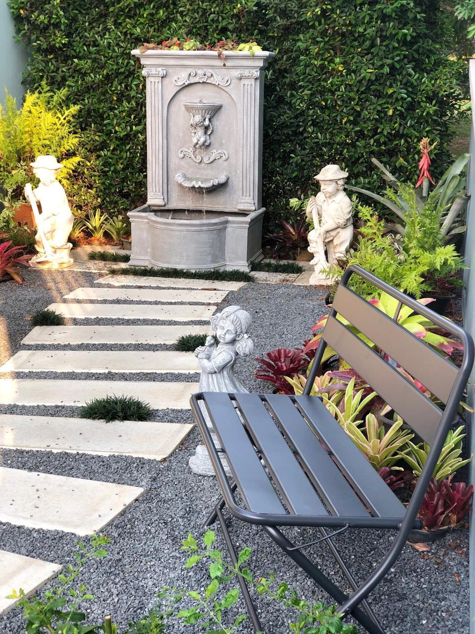 A garden with a stone fountain, statues, and a bench.